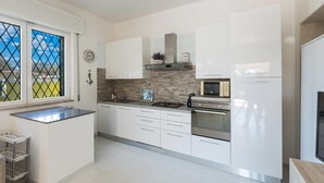 Eine moderne Küche mit weißen Schränken, einem Gasherd, einem Backofen und einer Mikrowelle. Ein Fenster bietet Blick ins Freie.