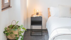 A bedroom with a bed, bedside table, lamp, and a potted plant.