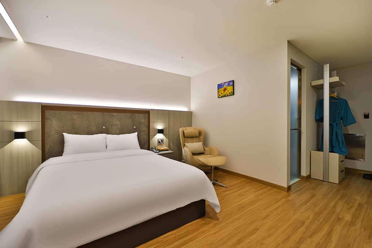 Moderni hotellihuone, jossa on suuri sänky, yöpöytä lampun kanssa, tuoli ja vaatekaappi.