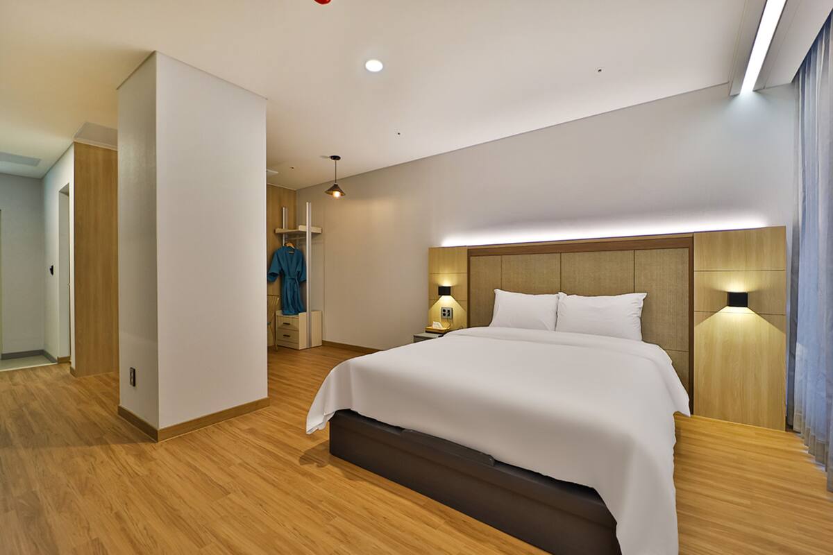 Moderni hotellihuone, jossa on suuri sänky, puulattia, yöpöytä lampun kanssa ja vaatekaappi.
