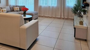 A modern living room with a beige sofa, a small round table, and a vase of red flowers. - Triima Inn Dayang Bay by Perfect Host (Langkawi)