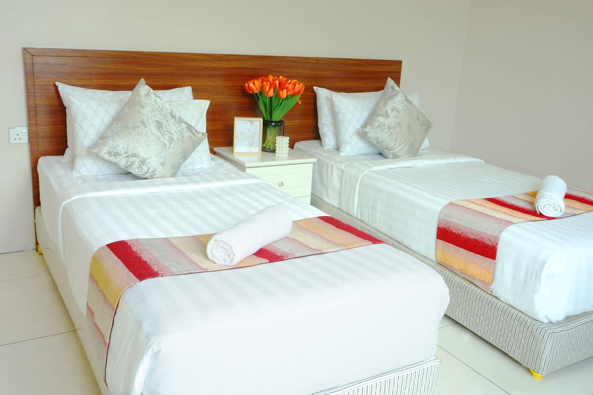 Habitación de hotel con dos camas, cabecera de madera, mesita de noche con un florero y una colcha a rayas.