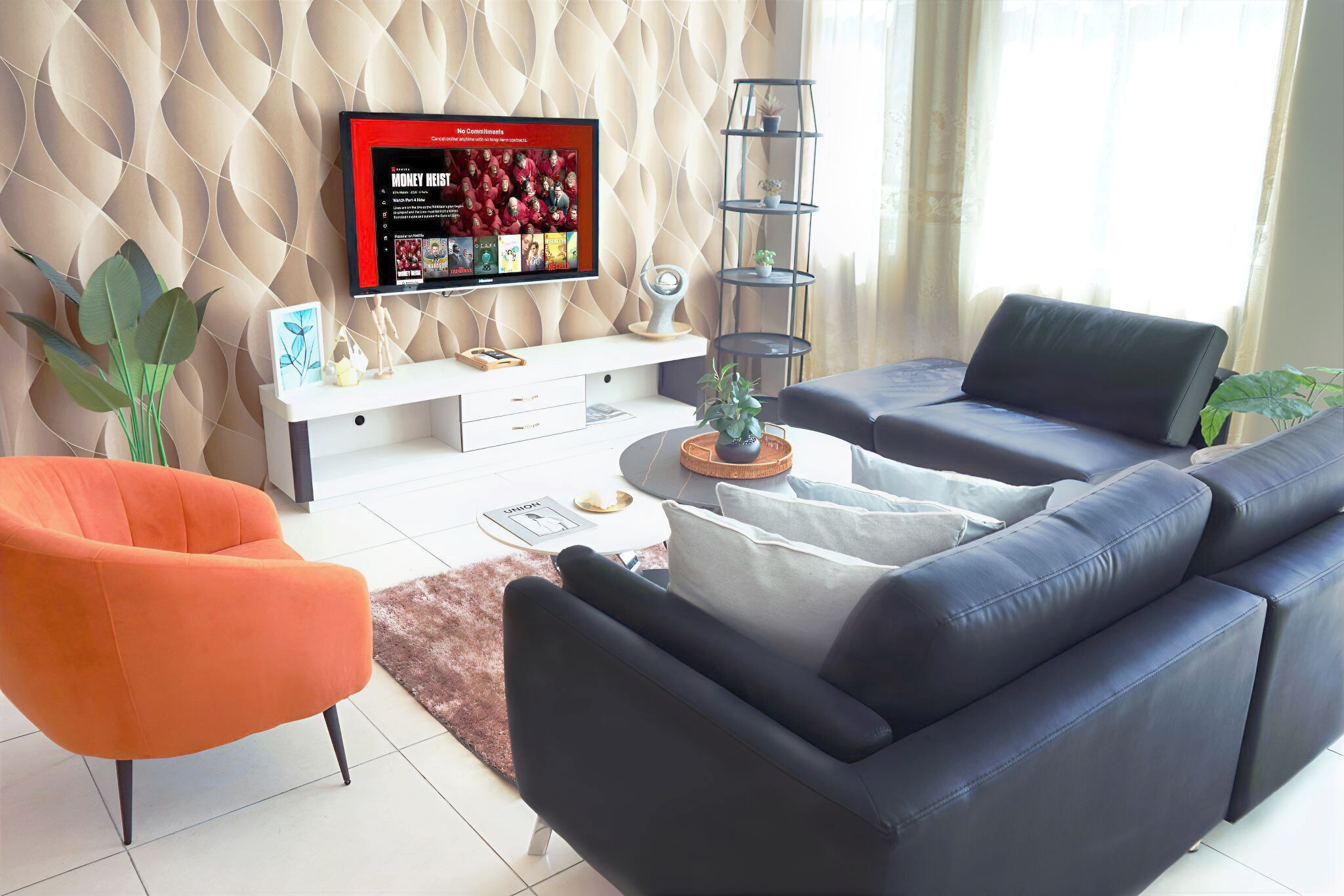A modern living room with a black leather sofa, an orange armchair, and a white console table with a flat-screen TV.
