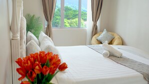 A neatly made bed with white linens, a rolled towel, and a vase of red flowers on a bedside table. - Triima Inn Dayang Bay by Perfect Host (Langkawi)
