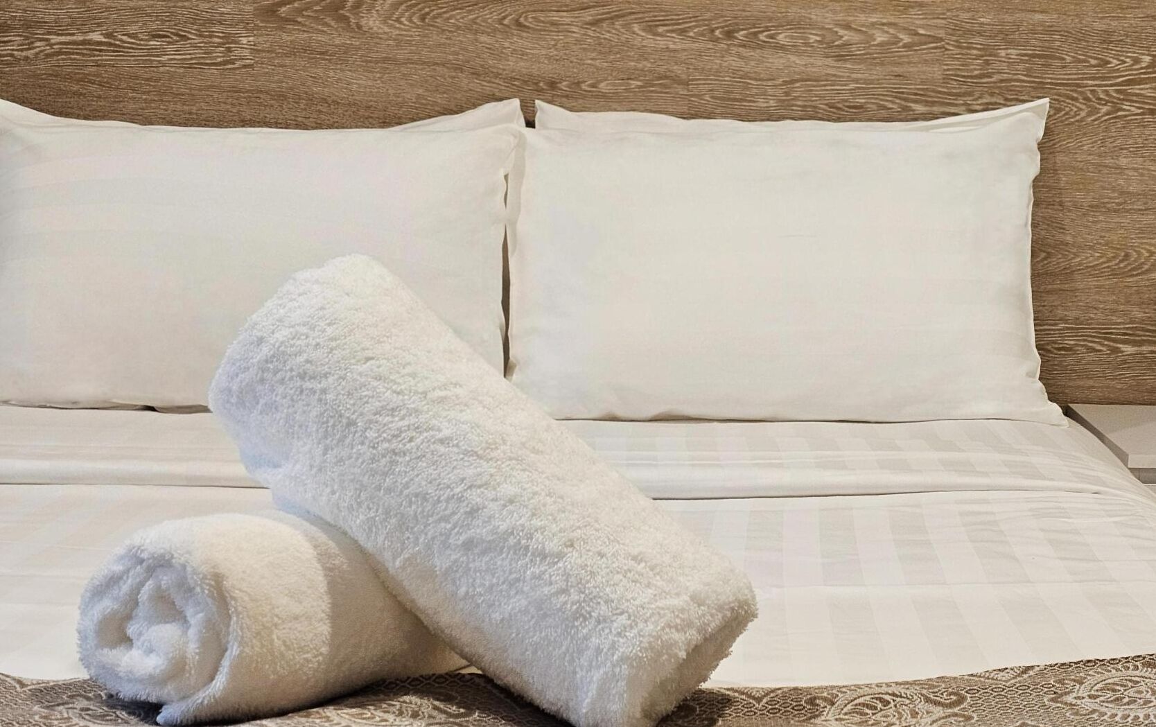 A neatly made bed with white linens and a rolled white towel on the side.