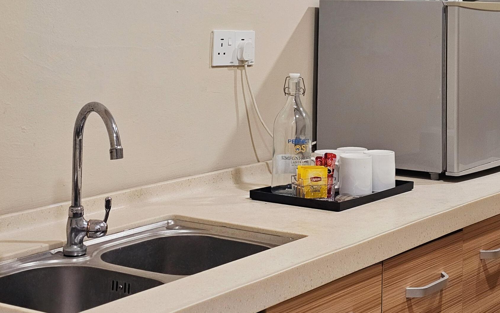 A kitchen with a double sink, a coffee maker, and a tray with coffee cups and condiments.