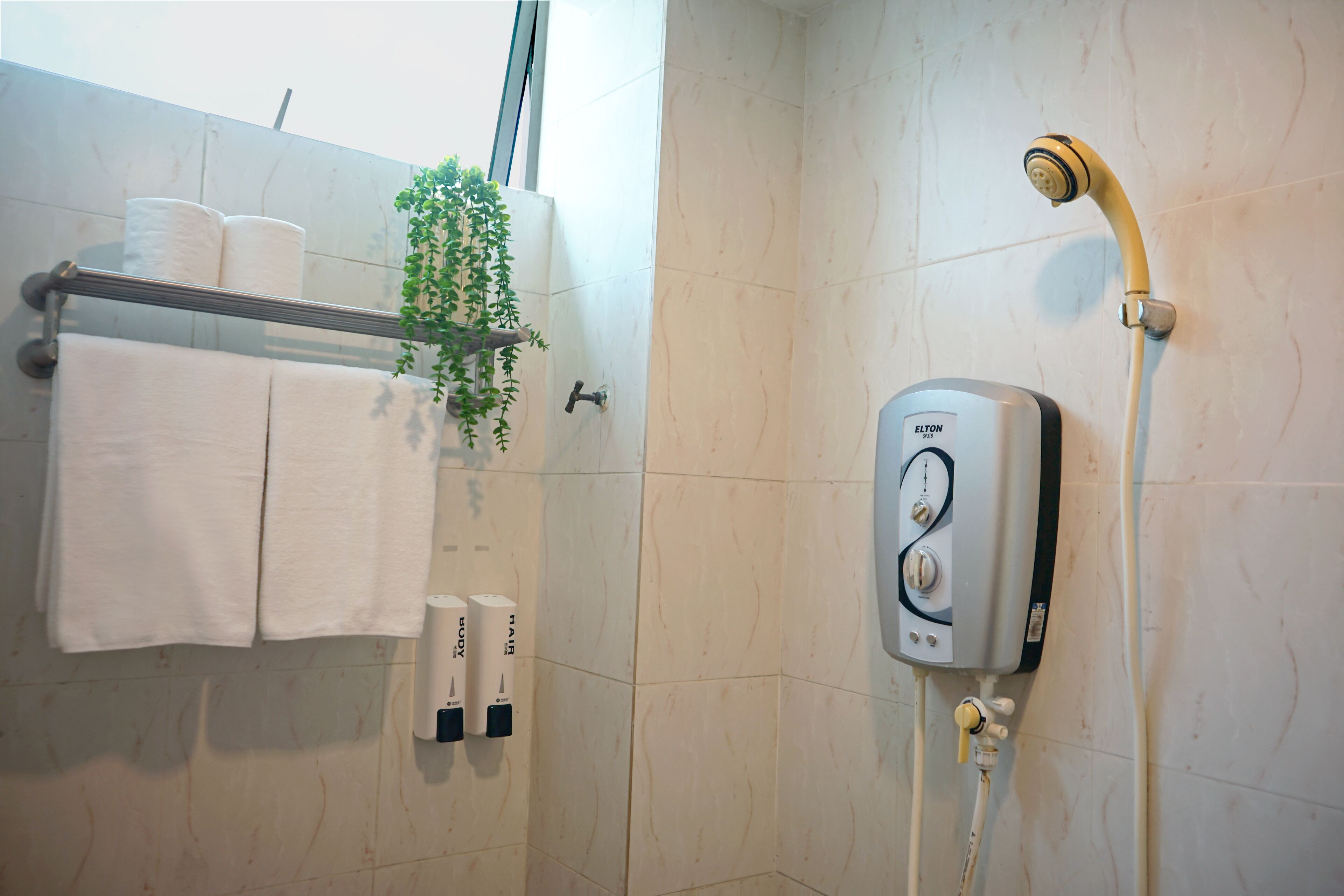 A bathroom with a glass shower enclosure, a towel rack with white towels, a plant, and a wall-mounted water heater.