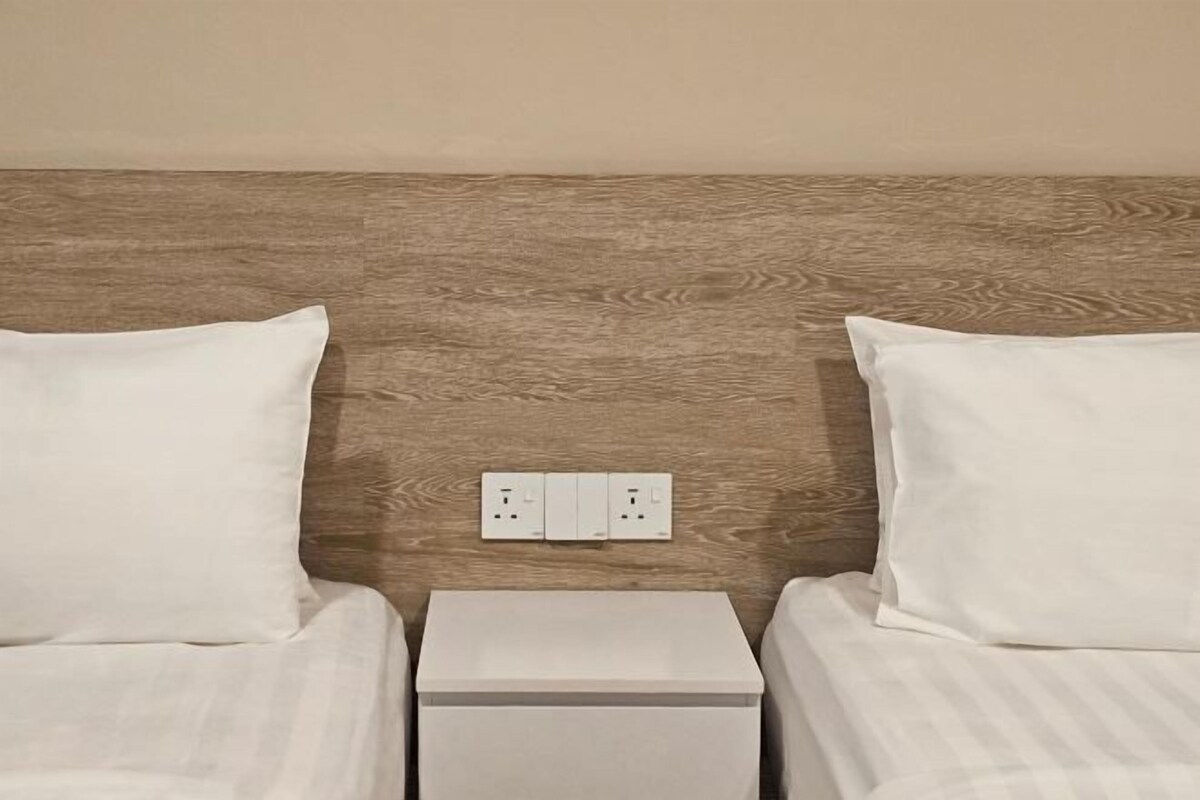A bedroom with two beds, a wooden headboard, and a nightstand with a power outlet.
