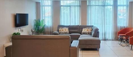 Ein modernes Wohnzimmer mit einer Eckcouch, einem Flachbildfernseher und einer Topfpflanze.