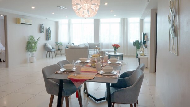 A modern dining area with a large table set for four, surrounded by chairs. There is a decorative light fixture above the table, and the room has a clean, minimalist design with white walls and a tiled floor. - Triima Inn Dayang Bay by Perfect Host (Langkawi)