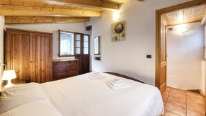 Una camera da letto con soffitto in legno, un letto con lenzuola bianche, un armadio in legno, una finestra con vista e un quadro appeso al muro.