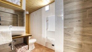 Un bagno con soffitto in legno, un lavabo bianco, un water e una zona doccia.