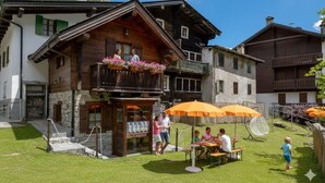 Un tradizionale chalet con facciata in legno, posti a sedere all'aperto e vista sulle montagne.