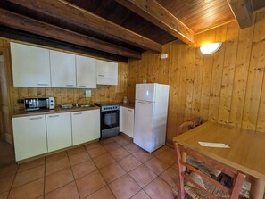 Une cuisine de taille réduite avec des murs en bois, un réfrigérateur blanc, une cuisinière, un four à micro-ondes et un évier.
