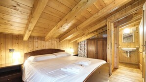 Un dormitorio tipo cabaña de madera con cama, mesita de noche, armario y baño con lavabo y espejo.