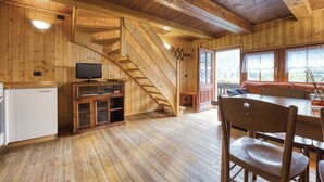 Interior de una cabaña de madera con zona de cocina, una mesa de comedor y una escalera.