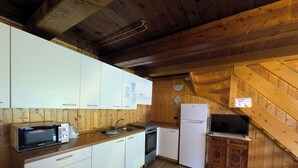 Una cocina con paredes de madera, armarios blancos, un microondas, un fregadero, un lavavajillas, un refrigerador y un televisor sobre un mueble de madera.