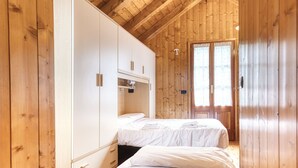 A wooden-paneled room with two single beds, a wardrobe, and a window with curtains.