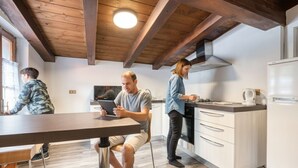 A modern kitchen with wooden beams, a dining area with a table, and a person using a tablet.