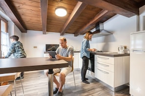 A modern kitchen with wooden beams, a dining area with a table, and a person using a tablet. - Beautiful apartment for 6 people with WIFI, TV, balcony, pets allowed and panoramic view (Isella)