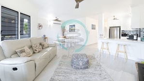 A modern living room with a sofa, ottoman, and a ceiling fan. - Nightcliff Foreshore Seaview Pool Workspace (Rapid Creek)