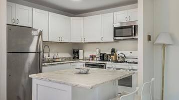 A modern kitchen with white cabinets, stainless steel appliances, a marble island, and a floor lamp.