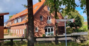 Ein rotes Backsteingebäude mit einem geneigten Dach und zahlreichen Fenstern. Ein Wegweiser zeigt die Richtung nach Altenberge, Nordwalde, Greven und Gimbte.