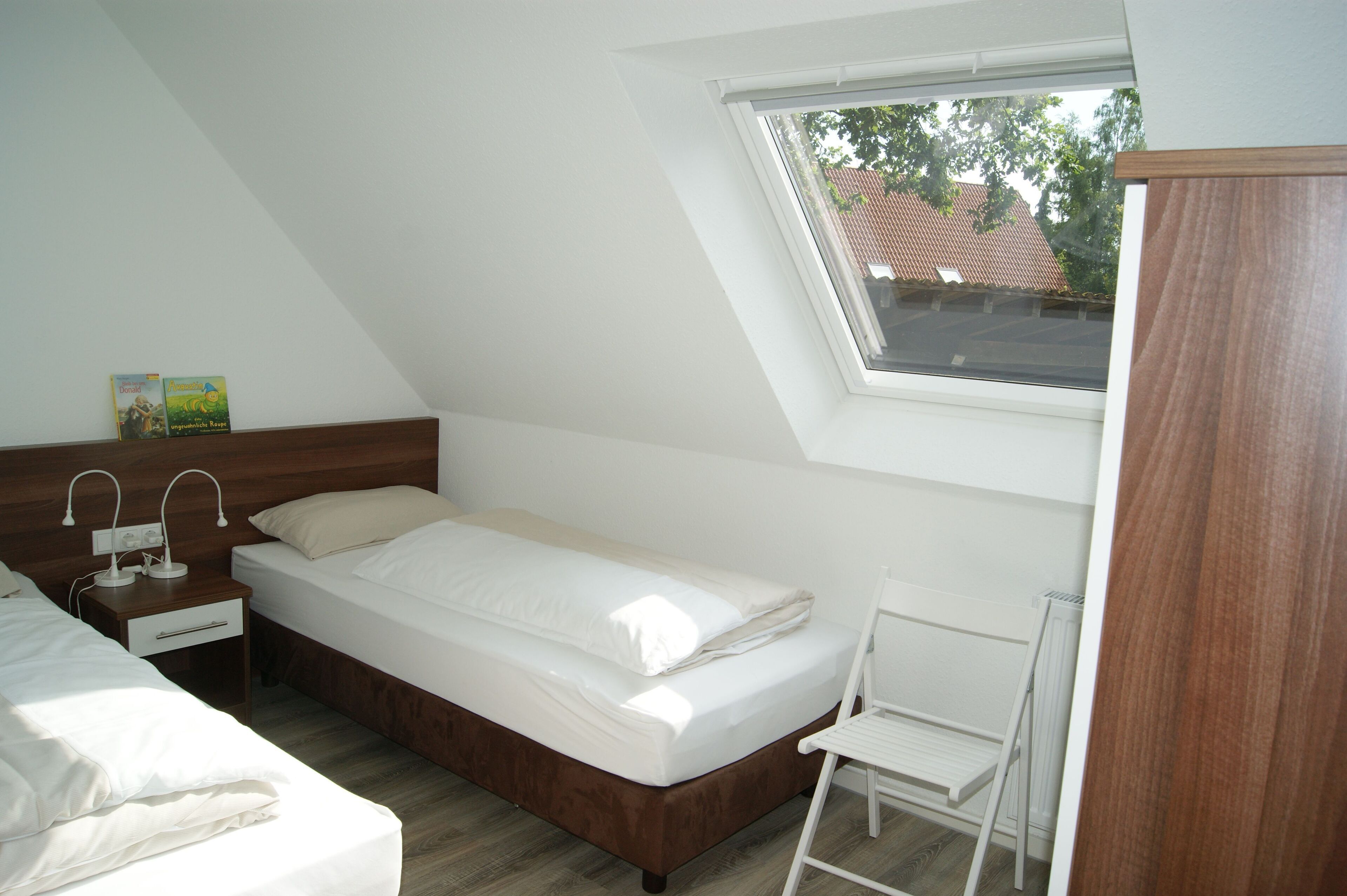 A bedroom with a single bed, a nightstand, a desk, and a chair.