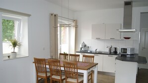 Une cuisine moderne avec des meubles blancs, une table à manger avec des chaises, un four à micro-ondes et une fenêtre agrémentée d’une plante.