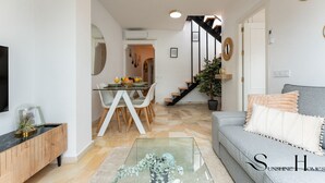 Un salon moderne avec un canapé gris, une table basse en verre et un escalier menant à un espace repas.