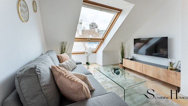 Un salon moderne avec un canapé gris, une table basse en verre, un meuble TV en bois et une lucarne.