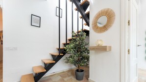 Un escalier avec des marches en bois et des rampes noires, une plante en pot, un tableau encadré et un miroir décoratif accroché au mur.