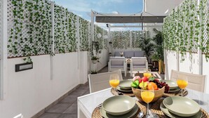 Un espace de restauration en plein air avec une table dressée pour quatre personnes, entouré de murs blancs recouverts de lierre.