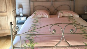 A bedroom with a metal bed frame, floral bedding, a wooden ceiling, and a nightstand with a lamp.