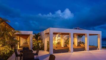 An outdoor seating area with tables and chairs, a covered structure with a roof, and a view of the ocean.