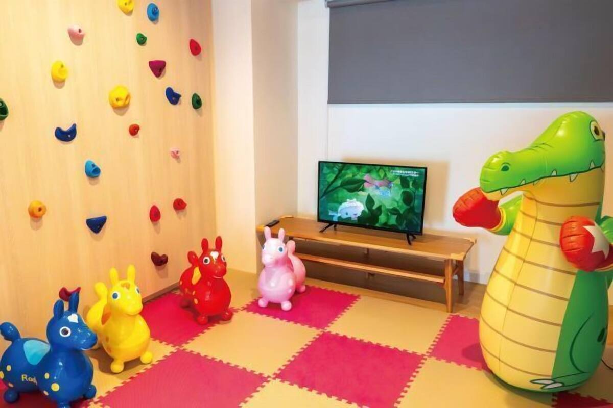Une pièce avec un mur d’escalade aux couleurs vives, une télévision et divers jouets.