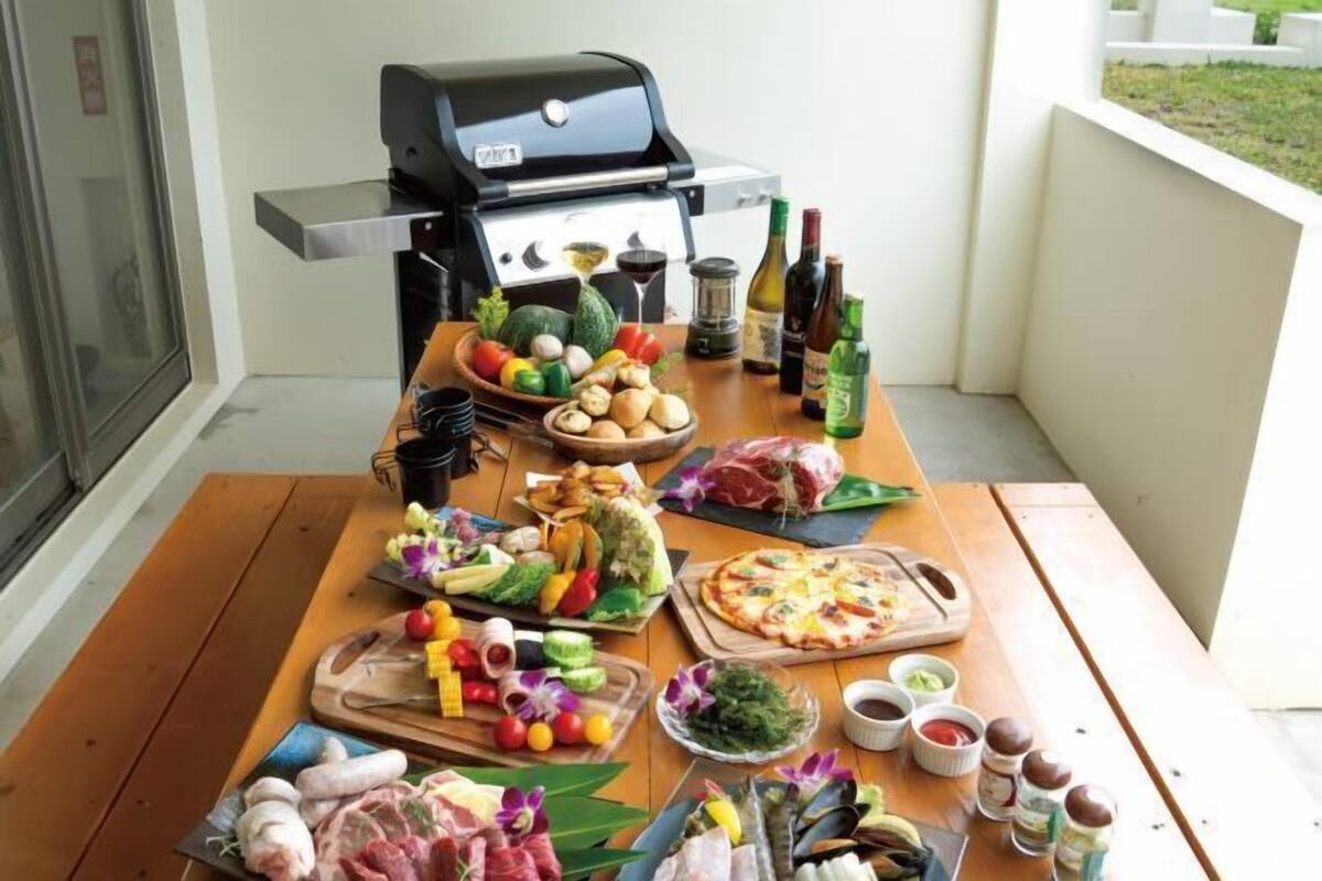 Une table en bois, sur laquelle sont disposés divers aliments, un barbecue et des condiments, sur un balcon.