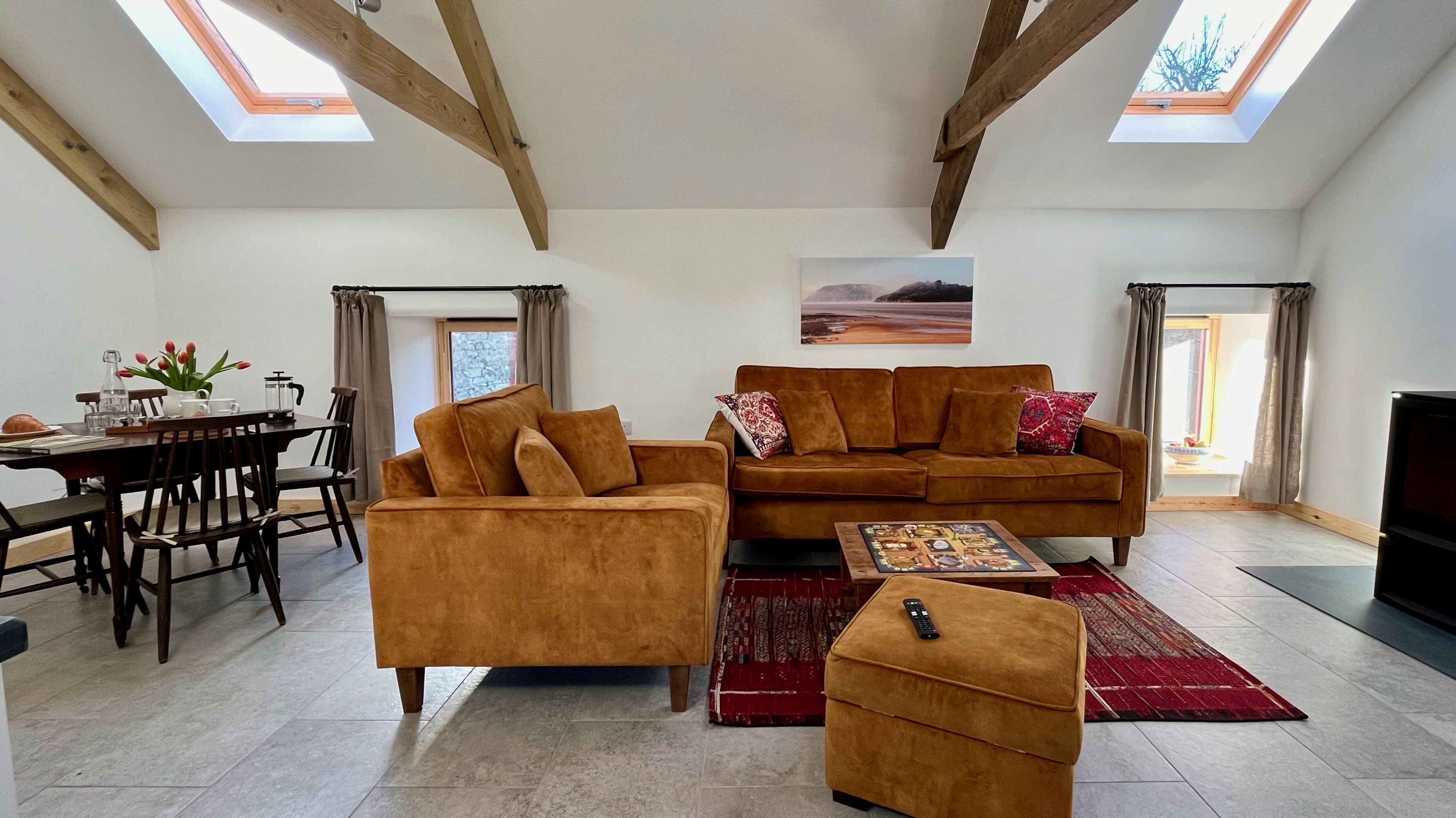 Un salon spacieux doté d’un haut plafond et de fenêtres de toit, aménagé avec un canapé, un pouf et une table basse.