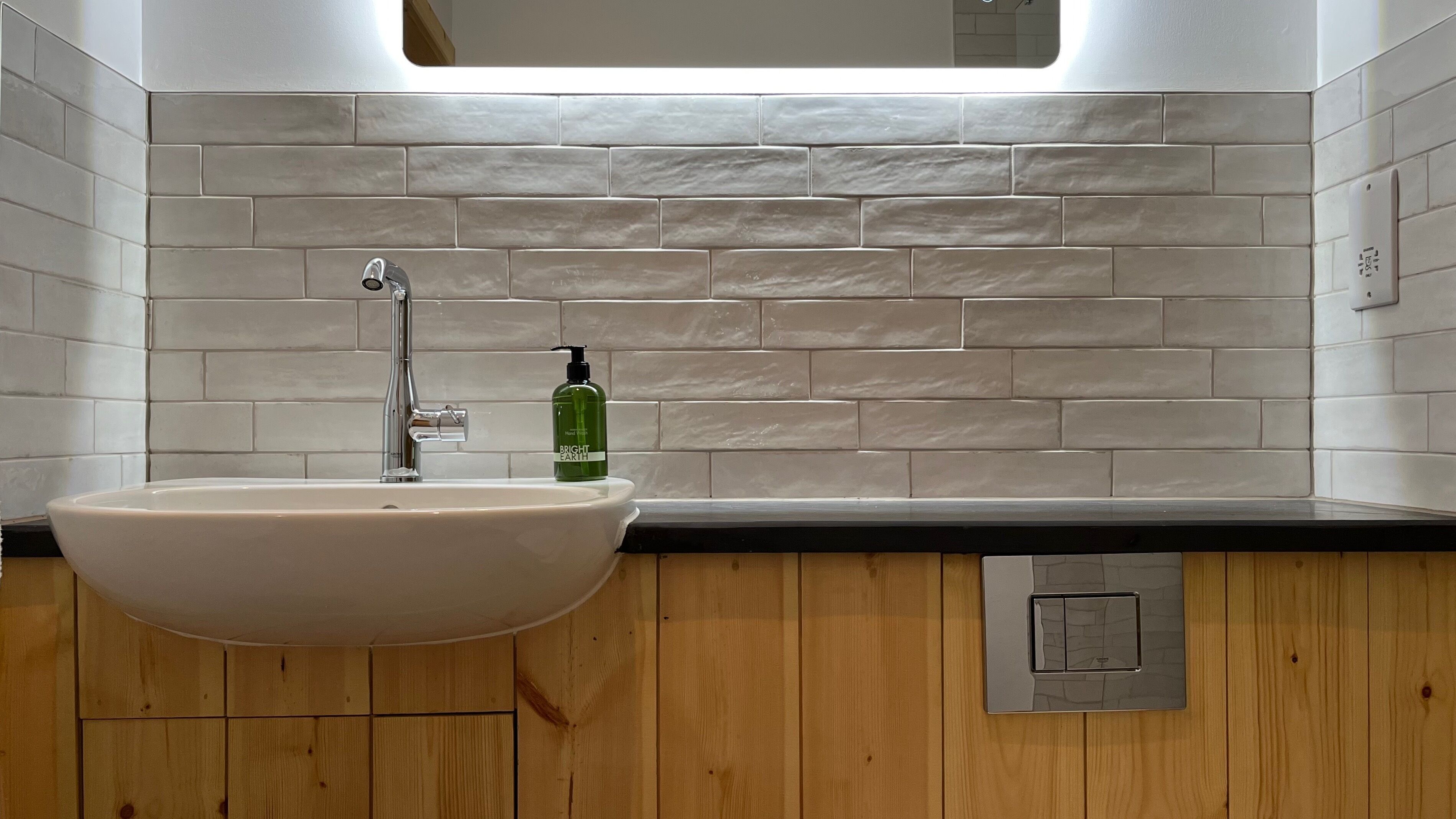 Un baño con lavamanos blanco, espejo encima y tocador de madera.