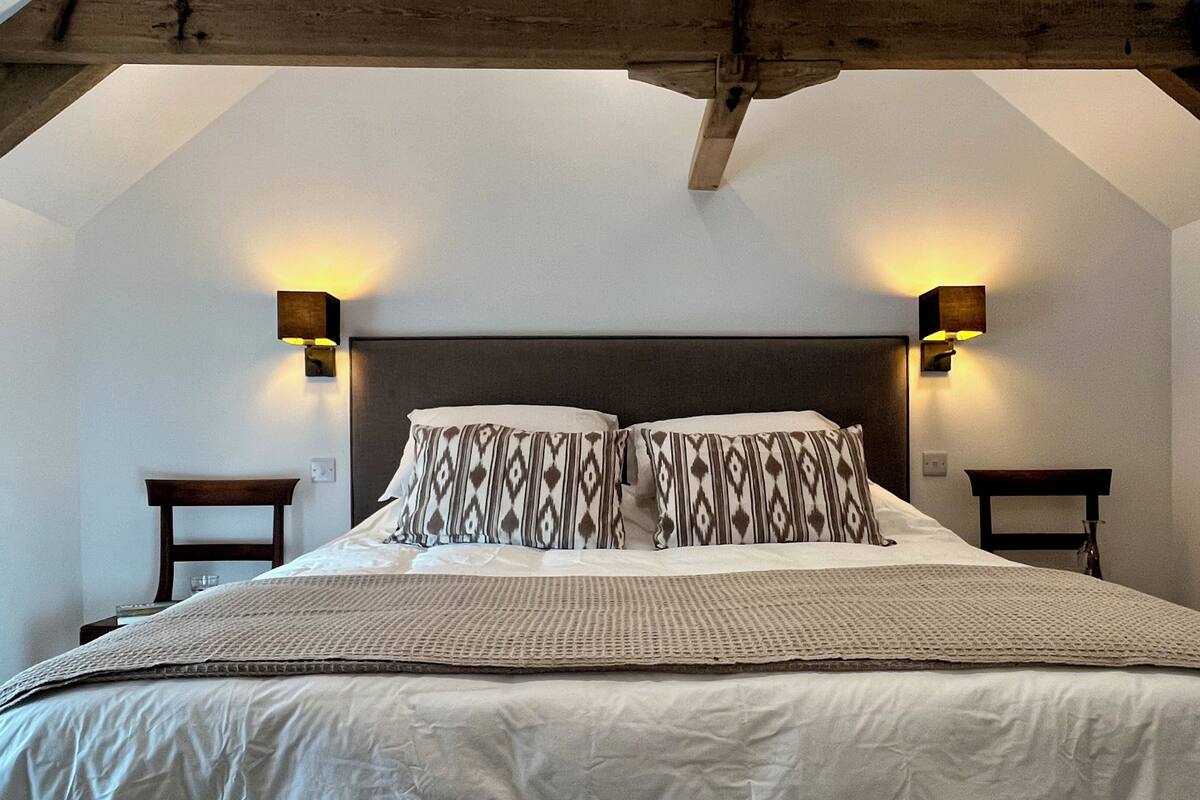 A bedroom with a large bed, two bedside tables, and wall-mounted lamps.