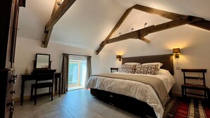 A bedroom with a large bed, wooden beams, a desk, and a mirror. - Cambrian Cottages (Pencader)