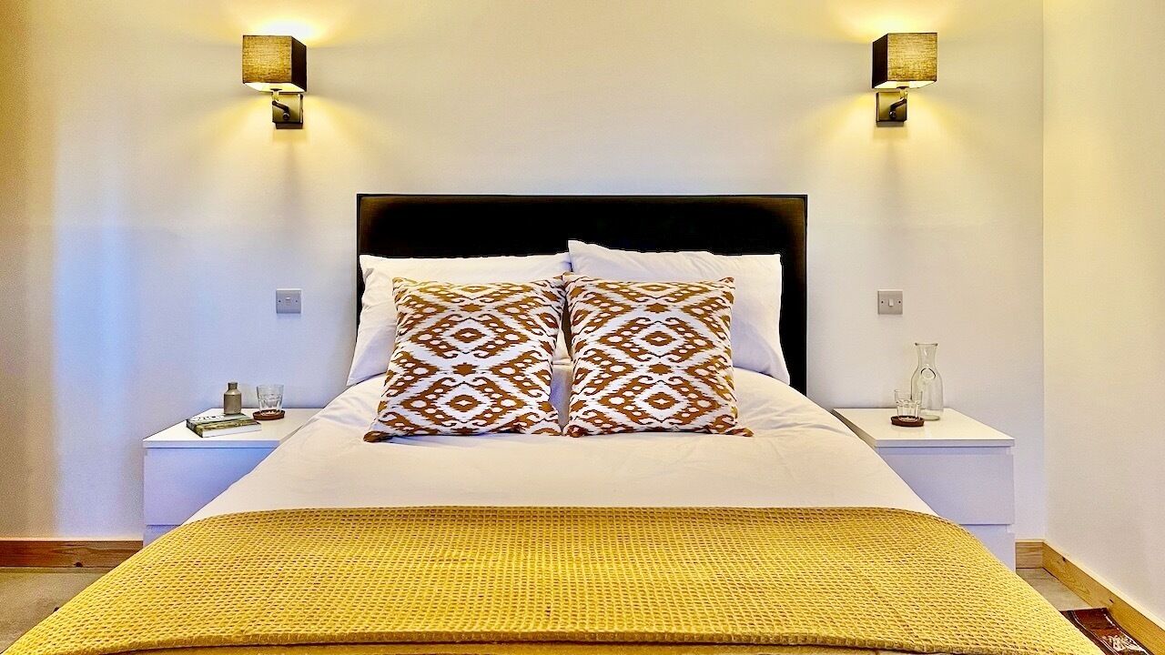 A neatly made bed with patterned pillows, two bedside lamps, and a bedside table with a glass and a book.