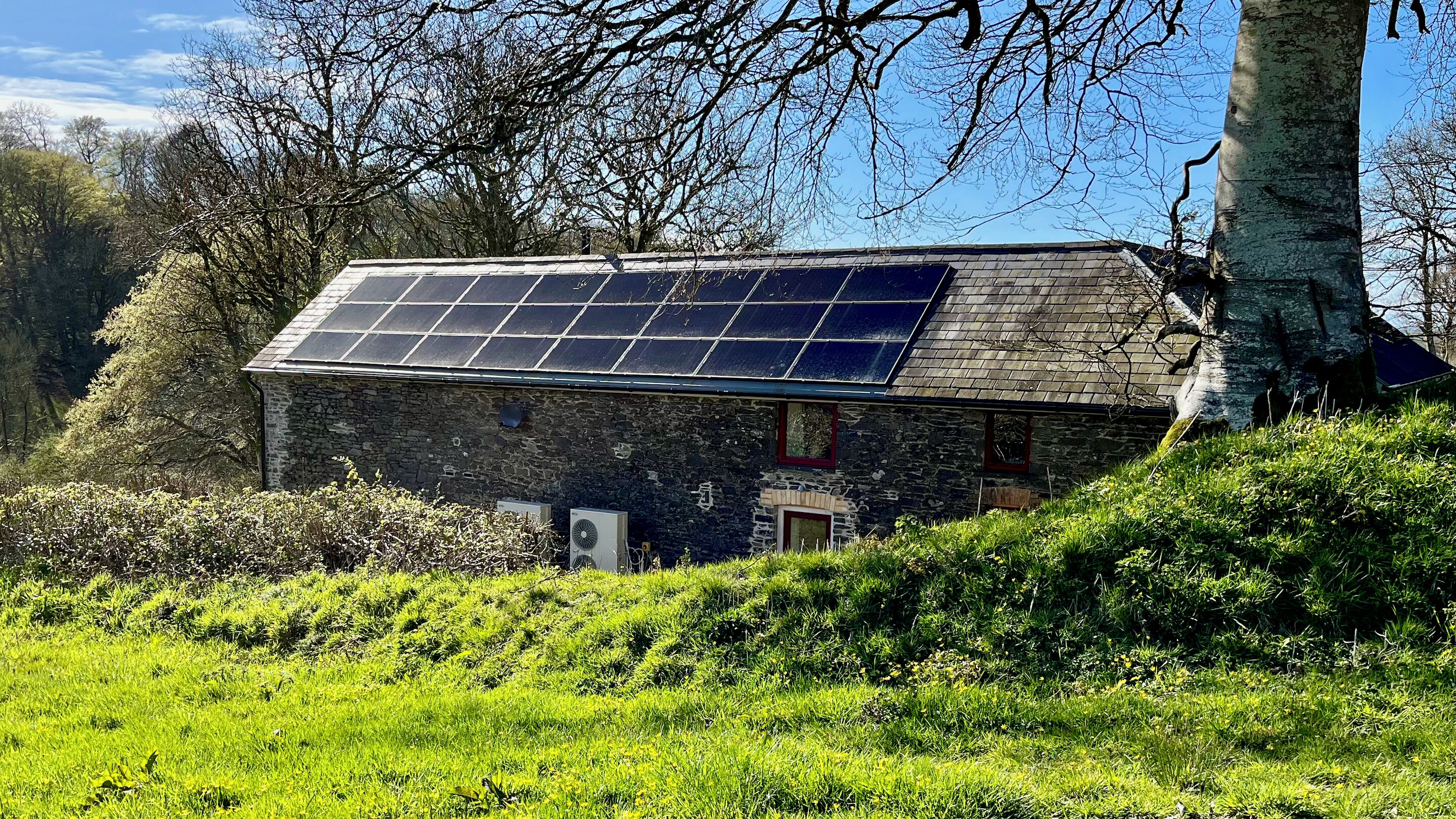 A stone building with a solar panel roof, surrounded by greenery and trees.