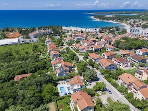 An aerial view of a coastal residential area with houses, a swimming pool, and a view of the sea.