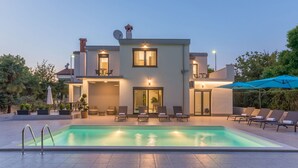 Ein modernes, zweistöckiges Haus mit Schwimmbad, Außenbereich zum Sitzen und einer gut beleuchteten Eingangspforte.