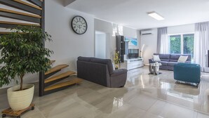 Ein modernes Wohnzimmer mit Treppe, einer großen Topfpflanze, einem grauen Sofa, einem blauen Sessel und einem Flachbildfernseher.