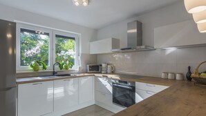 Eine moderne Küche mit weißen Schränken, einer Holzarbeitsplatte, einem eingebauten Backofen und einem Fenster mit Pflanzen.
