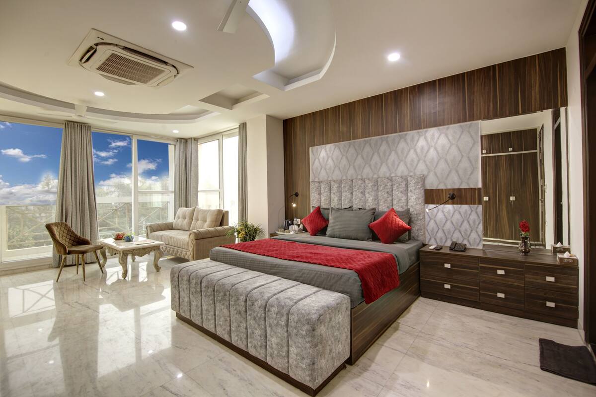 A modern bedroom with a large bed, a seating area, and a view of the sky.