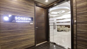 A reception area with a wooden panel wall, a reception desk, and a glimpse of a lounge with sofas and a coffee table. - SONESTA LUXURY APARTMENT (New Delhi)