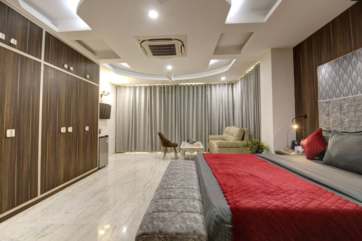 A modern bedroom with a large bed, a seating area, and a wardrobe.